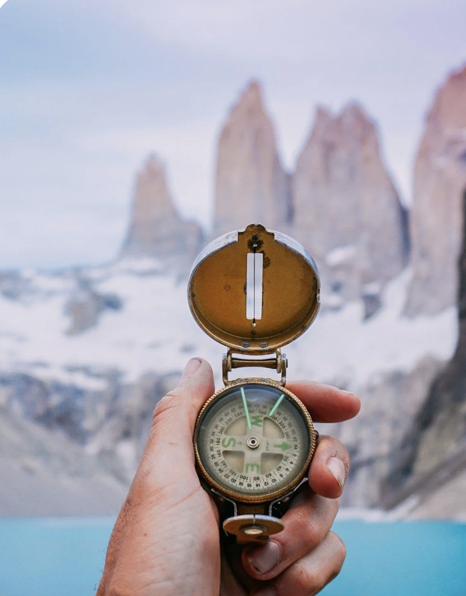Hand holding a compass in front of mountains